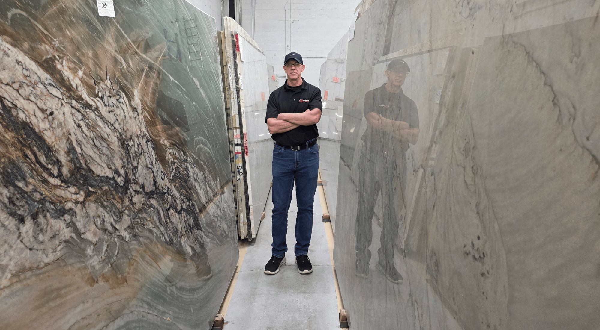 Carlos standing confidently between large marble slabs in a stone warehouse, representing strength, craftsmanship, and durability Carlos standing confidently between large marble slabs in a stone warehouse, representing strength, craftsmanship, and durability